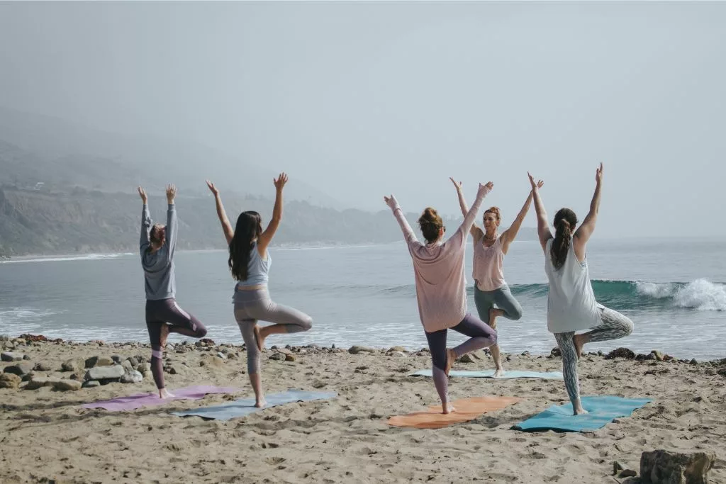 Pessoas praticando yoga em praia. Foto de Kaylee Garrett, Unsplash.